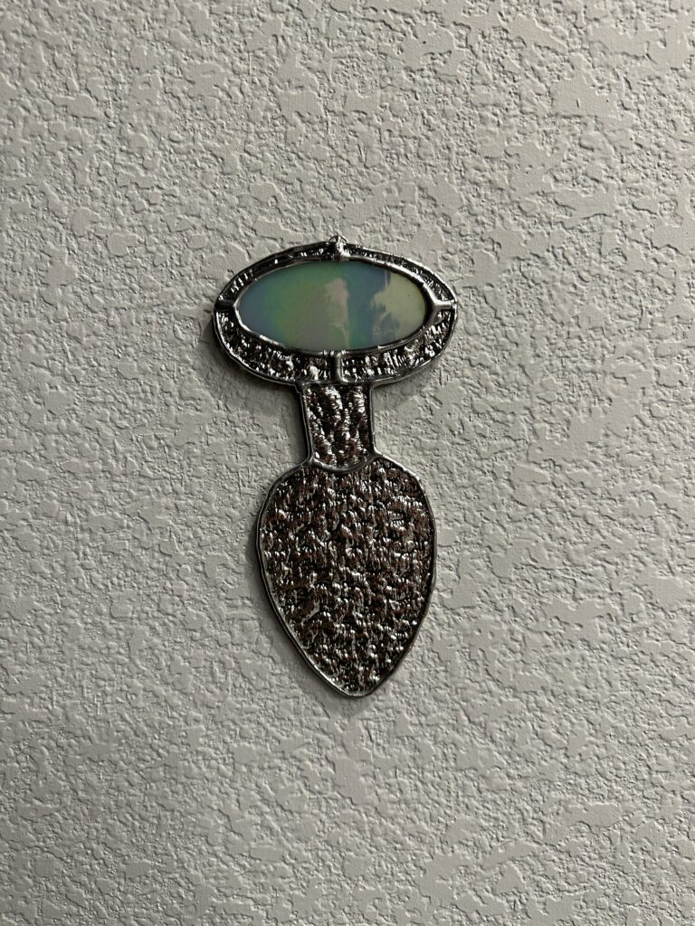 Metallic glass in the shape of a butt plug with an iridized opal green "jewel" at the end.
