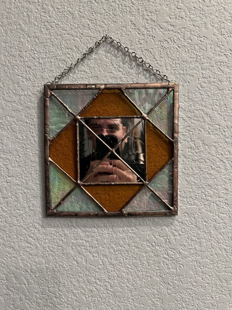 Square stained glass panel with iridized glass triangles in the corners and amber triangles in between. All around gold mirror glass.