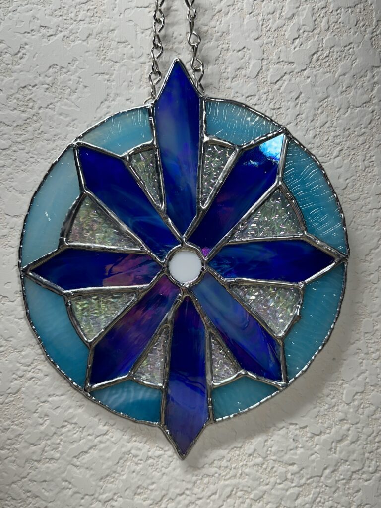 An 8-pointed dark blue star/snowflake inside of a light blue circle. There are clear iridescent triangles between the spokes. There is a white center dot.