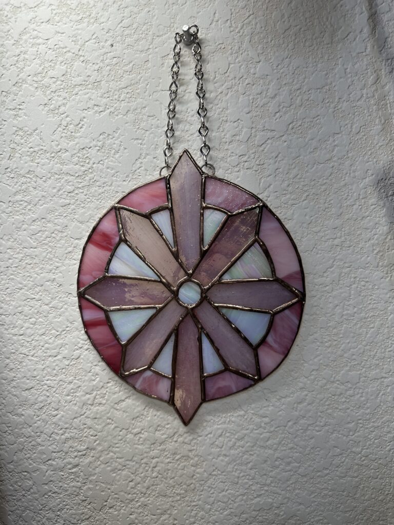 An 8-pointed pink star/snowflake inside of a pink circle. There are white iridescent triangles between the spokes. There is a white center dot.