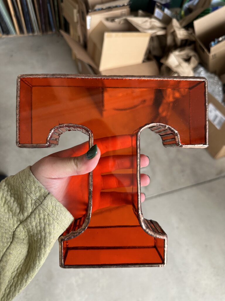 3-D orange letter "T" being held up in a hand.